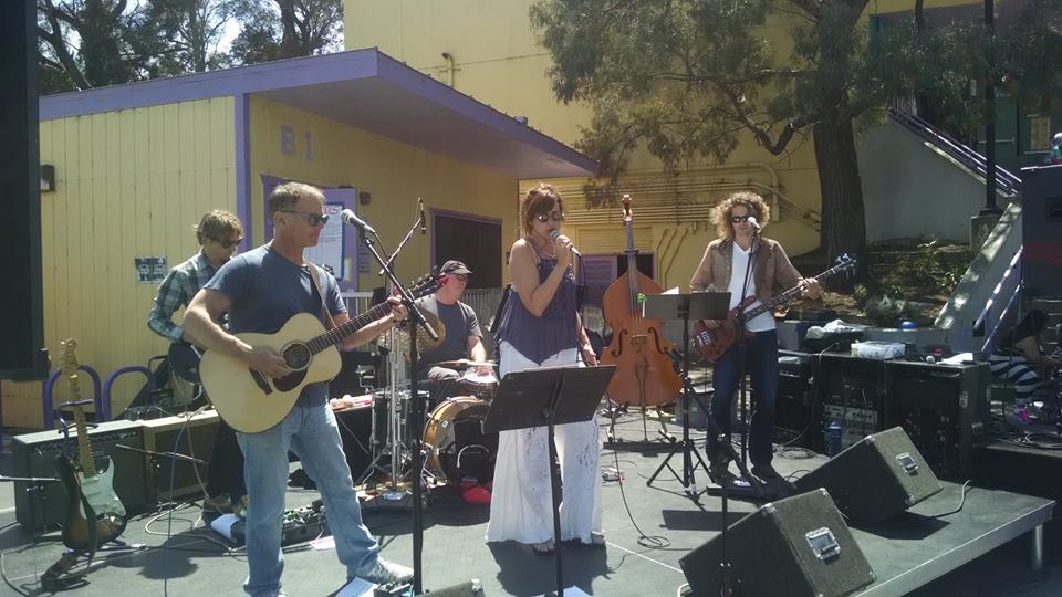 Sugar Ponies band on outdoor stage with microphones and PA system speakers